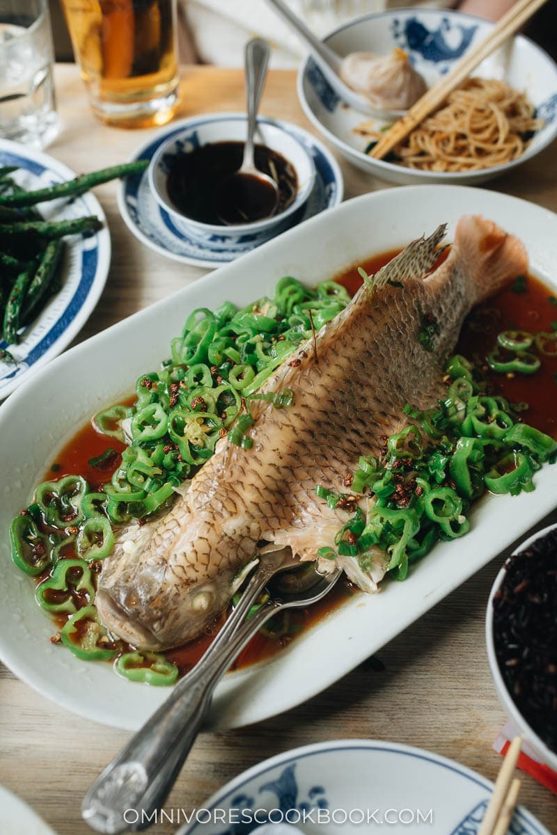 Whole steamed fish on a plate with chile peppers and soy sauce at Birds of a Feather